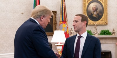 Donald Trump and Mark Zuckerberg shake hands in the Oval Office. A portrait of George Washington and military flags are visible in the background.