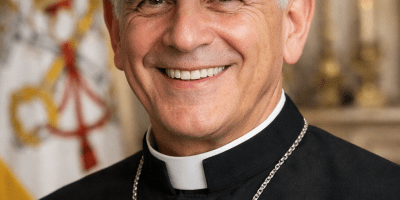 A smiling Catholic priest representing Pope Leo XIV wearing a black clerical shirt, silver cross, and a Chicago White Sox baseball cap against a Vatican-style background.