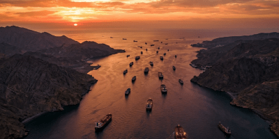 Cargo ships sailing through a narrow strait at sunset with rocky hills on both sides