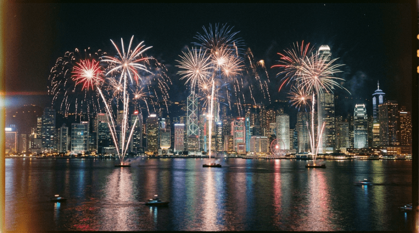 Fireworks bursting over a city skyline at night reflecting on harbor water