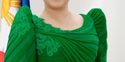 Official portrait of Philippine Vice President Sara Duterte smiling in a green formal dress, with the Philippine flag and vice-presidential seal displayed behind her.